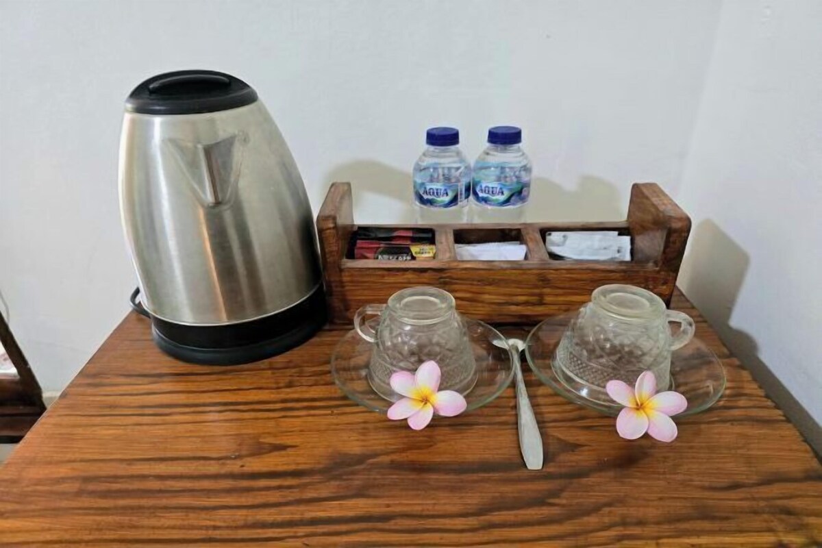 A stainless steel kettle, two glass teapots with floral decorations, two water bottles, and a wooden tray with a spoon on a wooden table.