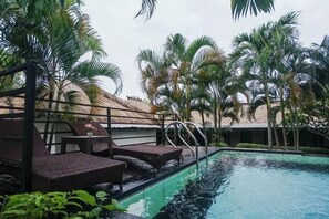 Un área de piscina con sillas de descanso y una estructura de techo de paja.