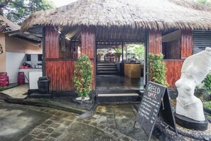 A rustic building with a thatched roof, a signboard, and a statue. - Kampung 168 Jimbaran Bali (Bali)