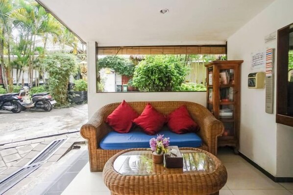 A room with a wicker sofa with red cushions, a glass coffee table, and a view of the outdoors. - Kampung 168 Jimbaran Bali (Bali)