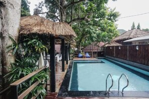 A swimming pool with a wooden deck and a thatched-roof structure. - Kampung 168 Jimbaran Bali (Bali)