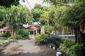 Un patio con un sendero empedrado, rodeado de abundante vegetación y una fuente decorativa.