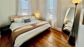 Une chambre à coucher avec un lit en bois, du linge de lit blanc, une lampe de chevet et une lampe sur pied.