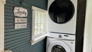 Une buanderie équipée d’un lave-linge et d’un sèche-linge Samsung, une fenêtre avec vue et un panneau indiquant : « Buanderie – fraîcheur et propreté garanties. »