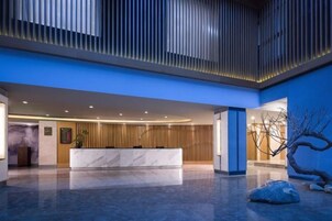 Un hall de hotel con una mesa de recepción, una planta grande y una escultura de árbol original.
