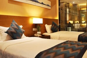 Ein Hotelzimmer mit zwei Betten, einem Nachttisch mit Lampe, einem Telefon und einer kleinen Pflanze.