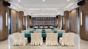 Un salón de conferencias con una larga mesa, sillas blancas y un escenario al frente.