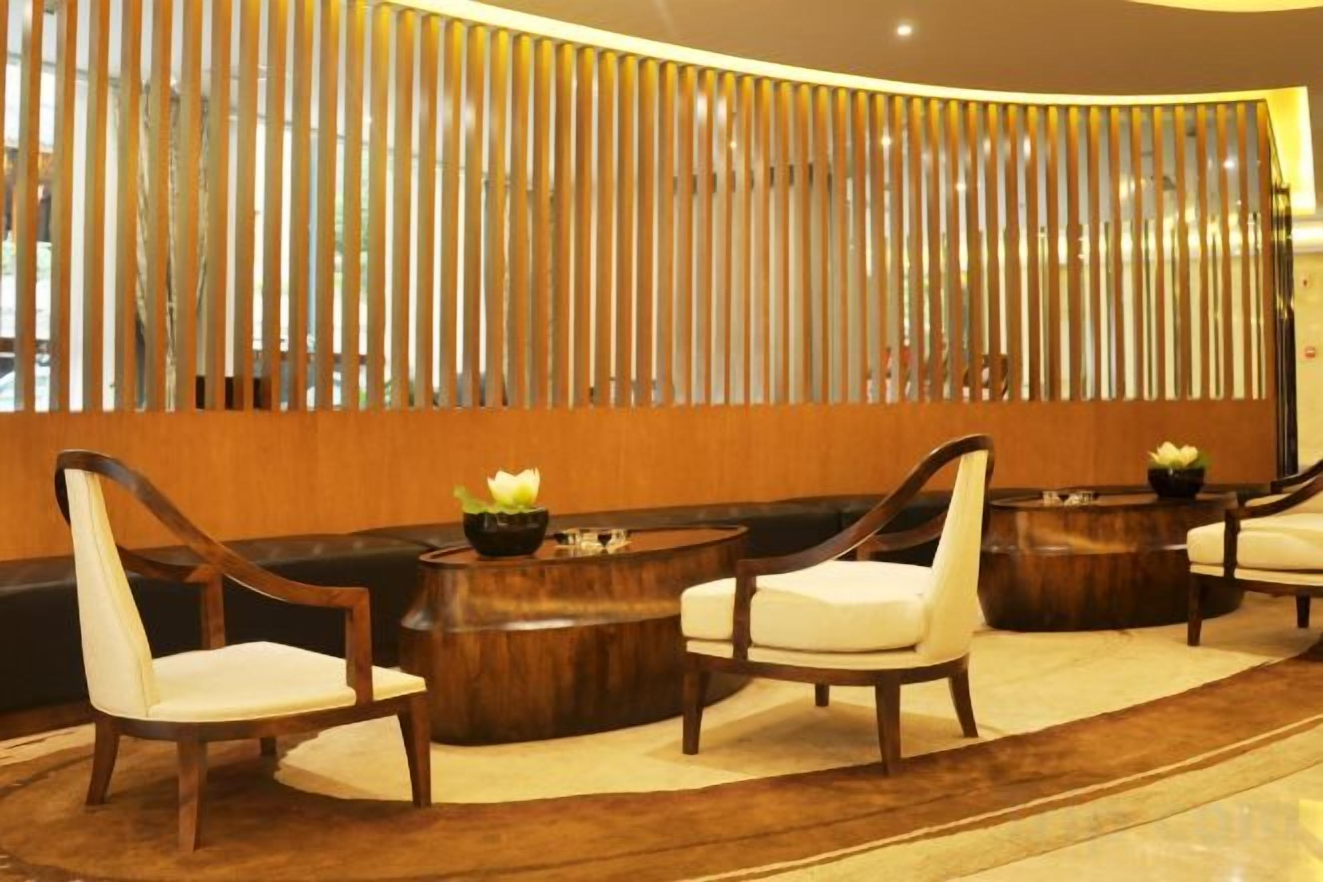 Un área de recepción con un mostrador de madera, dos mesas redondas de madera con sillas, y una pared decorativa con listones verticales.