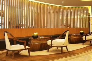 Un área de recepción con un mostrador de madera, dos mesas redondas de madera con sillas, y una pared decorativa con listones verticales.