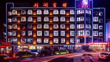 Un hotel de varios pisos con un letrero llamativo y varios vehículos estacionados en la entrada.