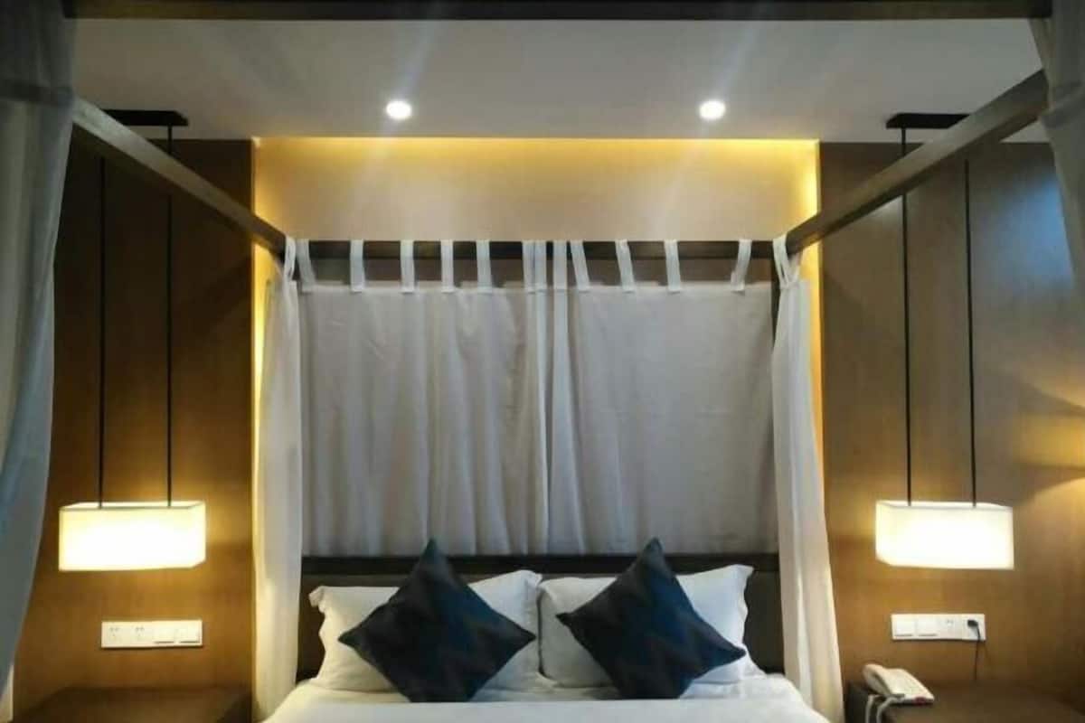 A hotel room with a bed, two bedside lamps, a telephone, and a curtain.