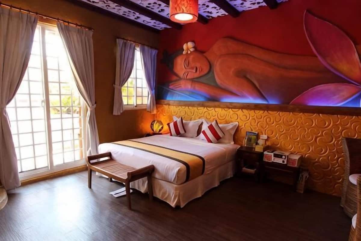 A hotel room with a bed, a chair, a nightstand, and a wall mural.