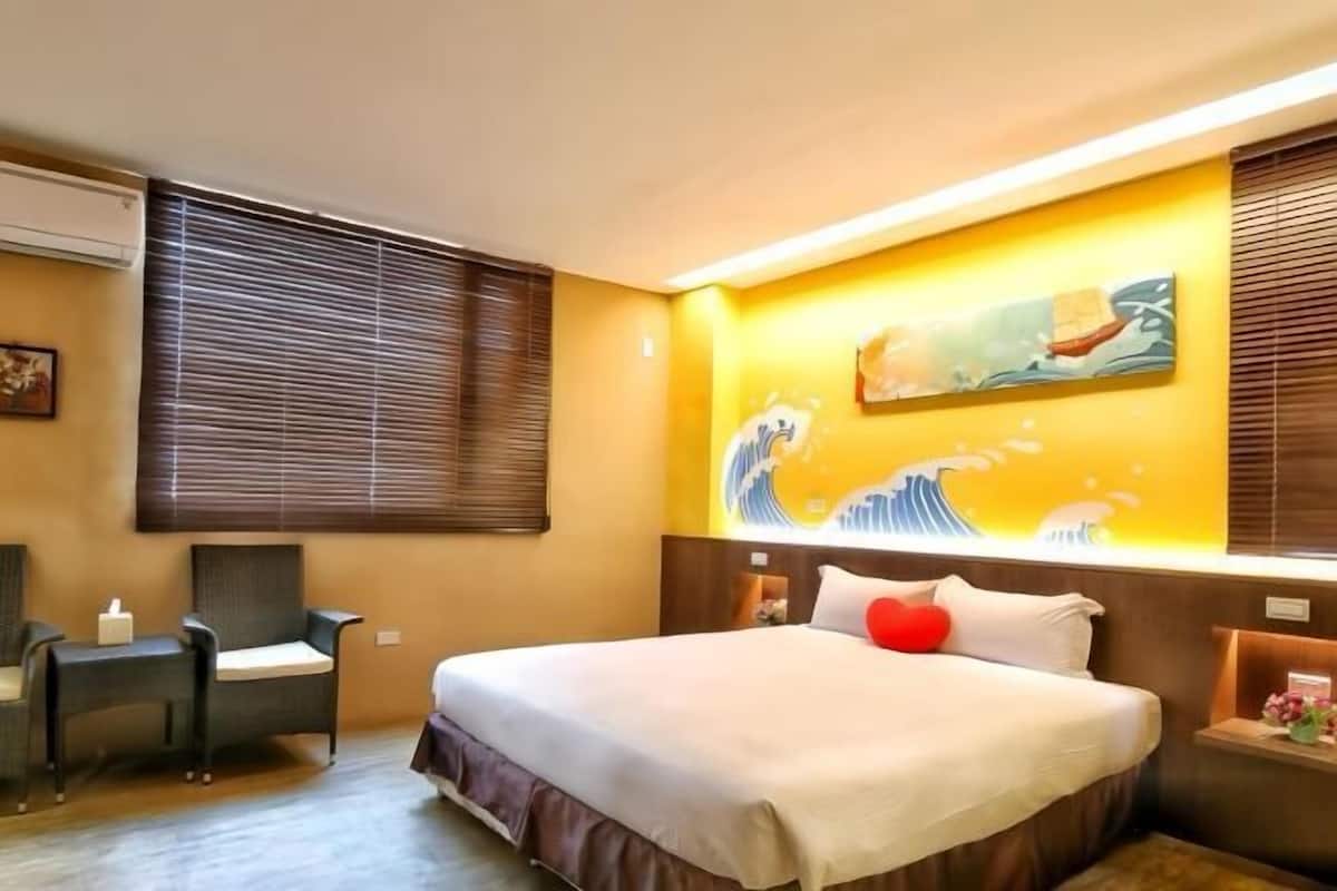 A hotel room with a bed, a chair, a bedside table, and a wall with a painting.