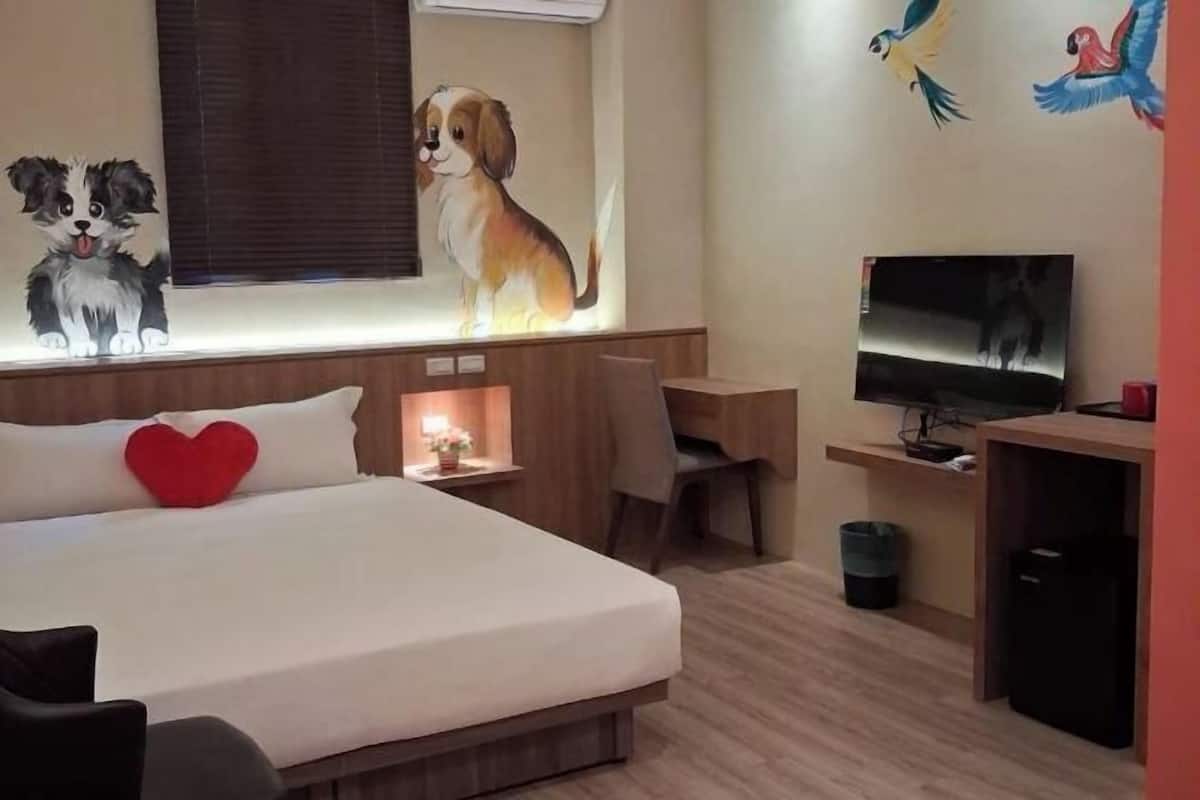 A hotel room with a bed, a desk, a TV, and artwork on the walls.