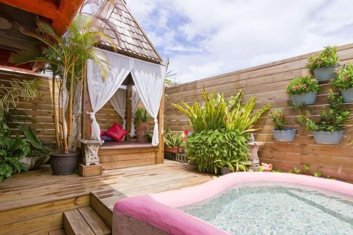 A wooden deck with a hot tub, a gazebo, and potted plants.