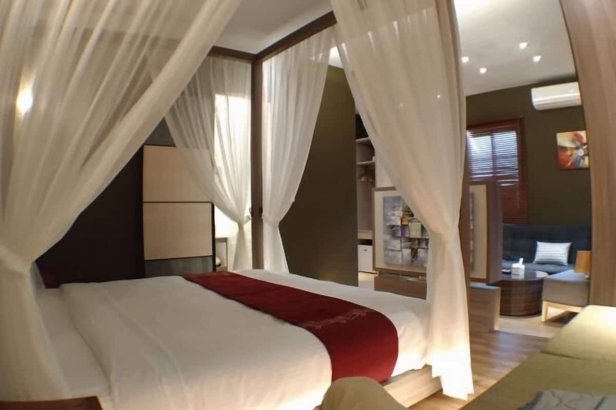 A bedroom with a large bed, white curtains, and a red accent.