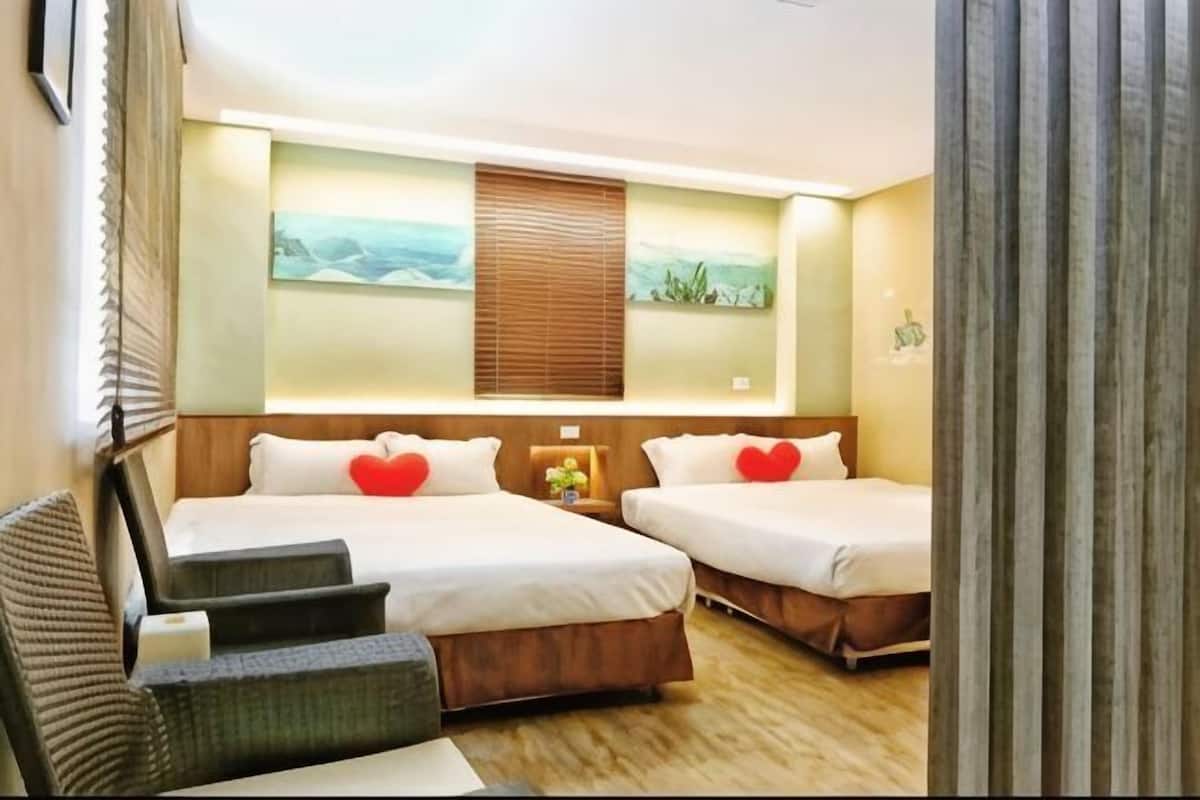 A hotel room with two beds, a sofa, a nightstand, and artwork on the walls.