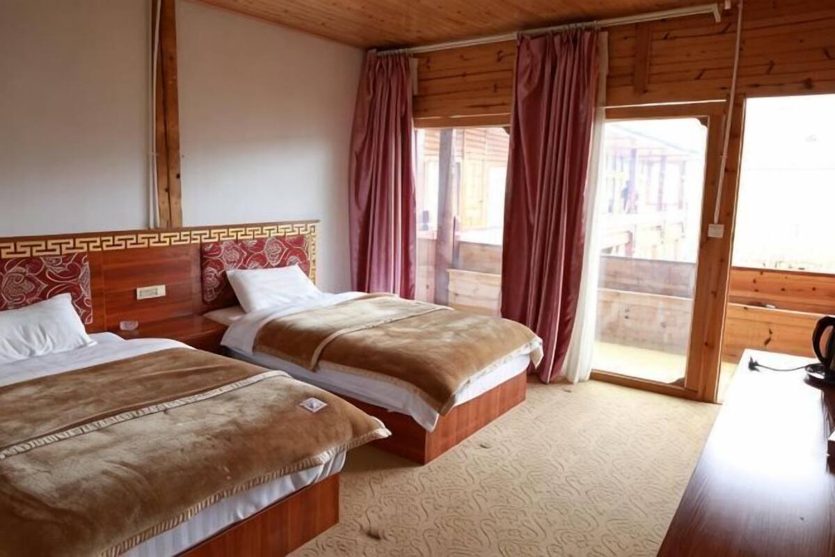Ein Zimmer mit zwei Betten, Holz-Kopfteilen, einem Holztisch und einer Schiebeglastür zu einem Außenbereich.