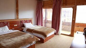 A room with two beds, wooden headboards, a wooden desk, and a sliding glass door leading to an outdoor area.