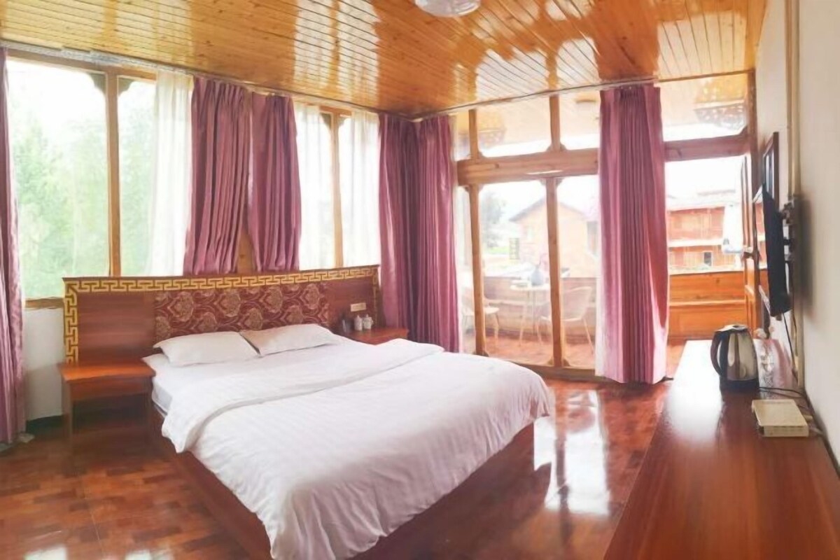 A wooden-paneled bedroom with a large bed, a bench, and a view of the outside.