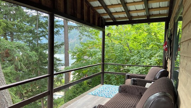 A covered outdoor seating area with a view of a lake and forest. - Small Cabin with gorgeous view and lake access (Nelson)