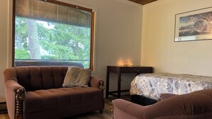 A cozy room with a brown sofa, a small table with candles, and a bed with a floral bedspread. - Small Cabin with gorgeous view and lake access (Nelson)