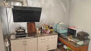 A compact kitchen with a stove, microwave, and a TV mounted on the wall. - Xujia Tingyuan Inn (Suzhou)