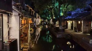 A narrow waterway flanked by traditional buildings with illuminated windows and a tree in the center. - Xujia Tingyuan Inn (Suzhou)