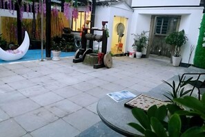 A courtyard with a crescent moon-shaped planter, potted plants, a table with a placemat, and a traditional water pump. - Xujia Tingyuan Inn (Suzhou)