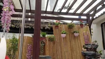 A covered outdoor area with bamboo walls, hanging plants, and potted plants.