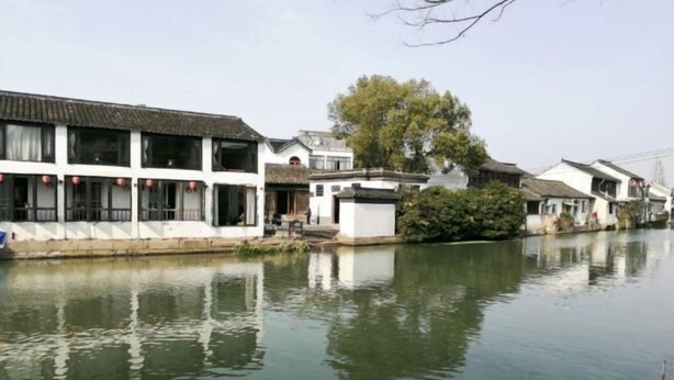 A traditional Chinese courtyard with white buildings, a calm water body, and a large tree. - Xujia Tingyuan Inn (Suzhou)