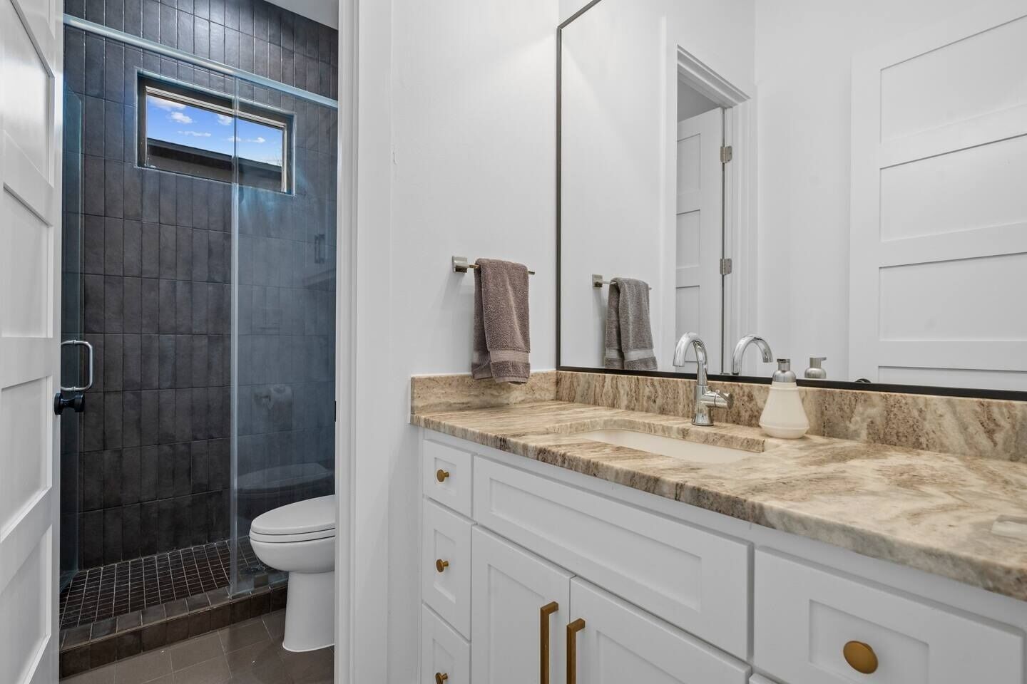 A modern bathroom with a glass shower enclosure, white cabinetry, and a marble countertop.