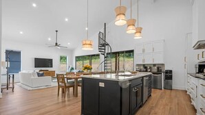 Un amplio espacio habitable con cocina central grande, suelo de madera y una escalera moderna.