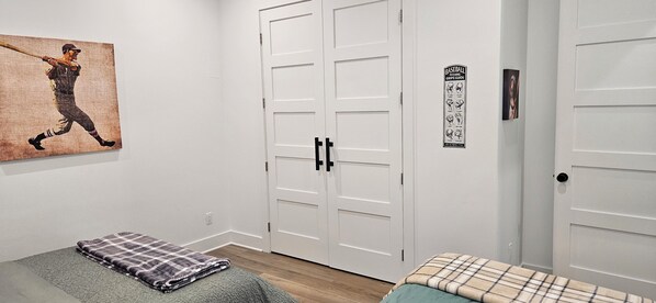 A bedroom with a bed, a bench, a painting, a closet, and a door with a baseball pitching guide.