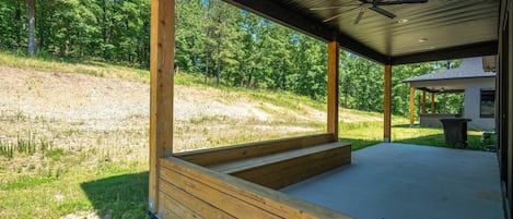A covered outdoor area with wooden steps leading to a concrete floor, surrounded by a grassy landscape and trees.