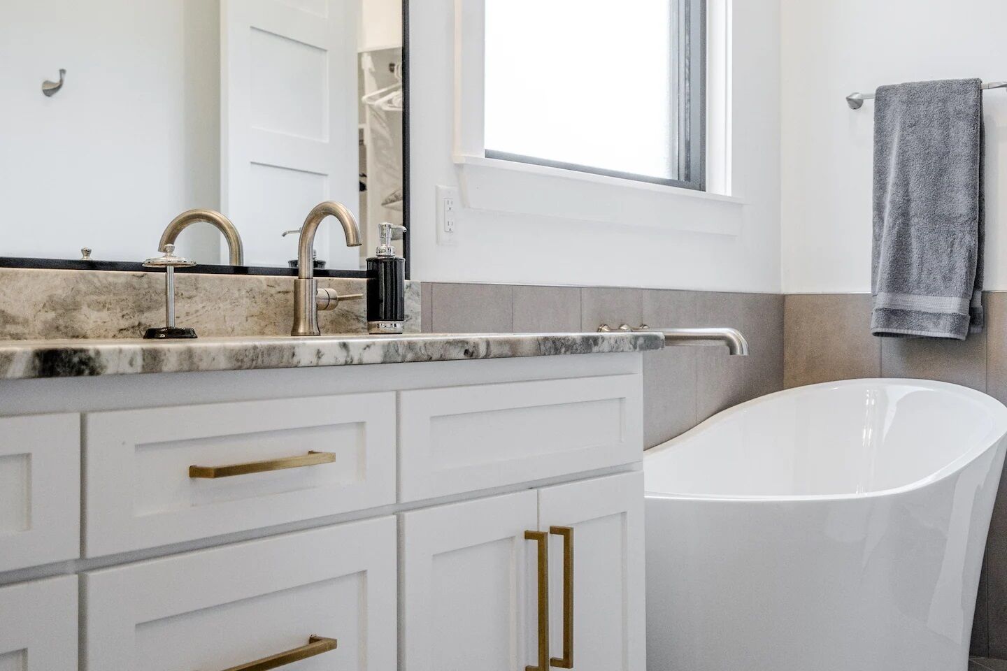 A modern bathroom with a freestanding bathtub, a vanity with a marble countertop, and a window providing natural light.