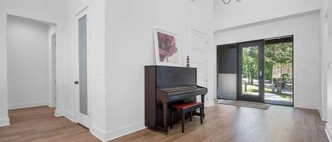 Une pièce spacieuse avec un grand piano, un parquet, un lustre et une grande porte-fenêtre coulissante donnant sur un espace extérieur.