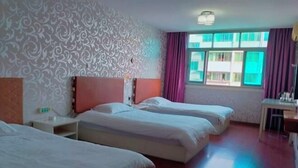 Een hotelkamer met drie bedden, een bureau en een raam met gordijnen.