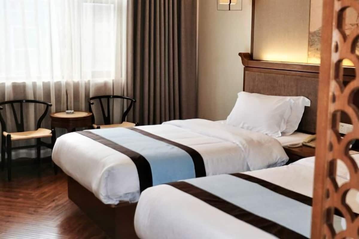 A hotel room with two beds, a small table, chairs, and a large window with curtains.