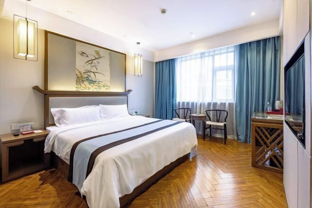 A hotel room with a large bed, a desk, chairs, a TV, and a painting on the wall.