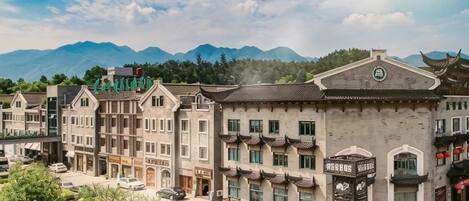 A hotel with traditional architecture, a parking area, and a mountainous backdrop.