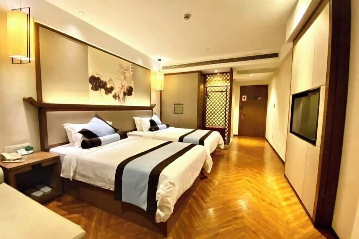 A hotel room with two beds, a TV, a wooden floor, and a decorative wall piece.