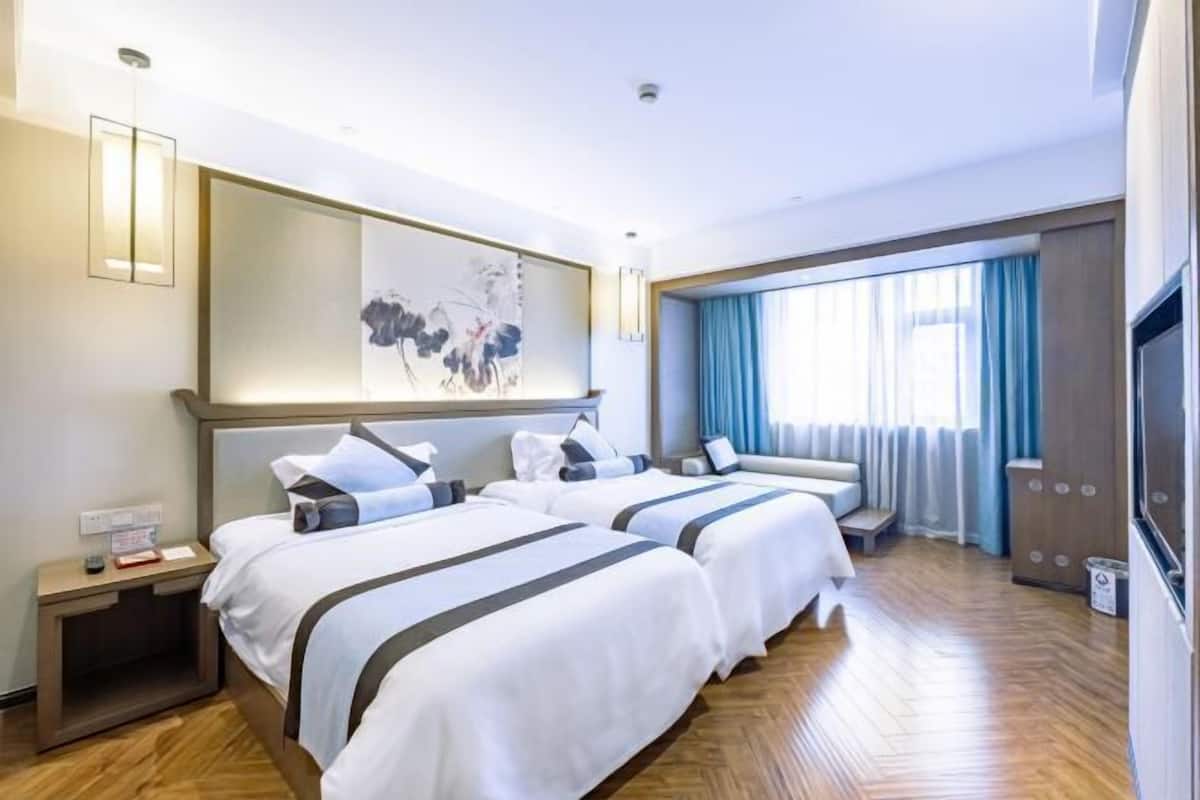 A hotel room with two beds, a large artwork on the wall, a TV, and a window with curtains.