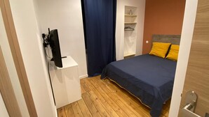 Une chambre à coucher avec un lit, un téléviseur posé sur un meuble, une armoire et une étagère avec des objets.