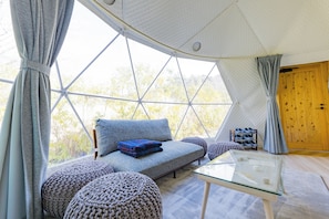 Um quarto aconchegante com sofá, pufes, mesa de vidro e porta de madeira.