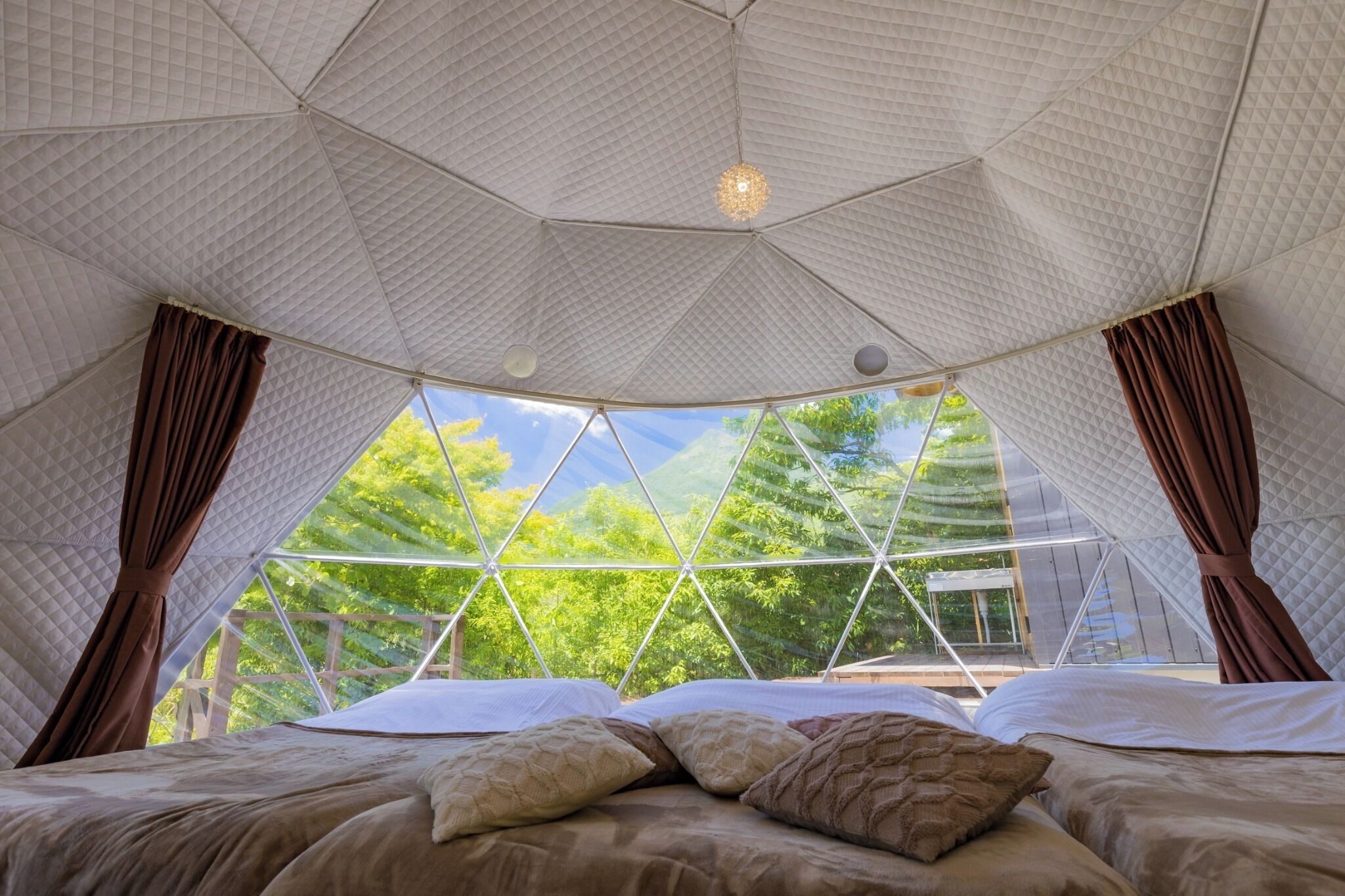 A tent-style room with a bed, curtains, and a view of trees.