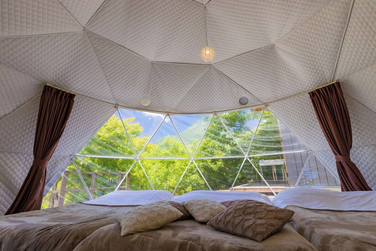 A tent-style room with a bed, curtains, and a view of trees.