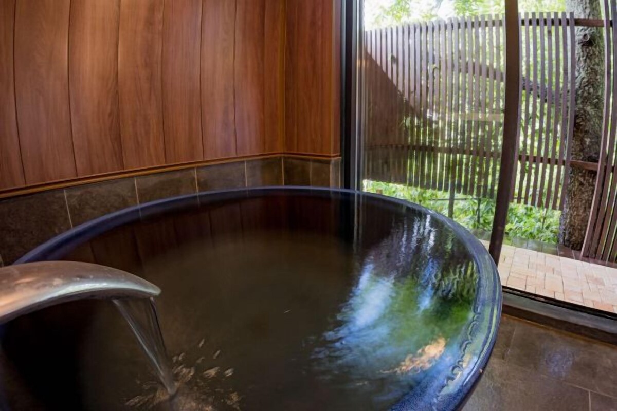 A hot tub with a metal faucet, surrounded by wooden paneling and a glass door leading to a garden.