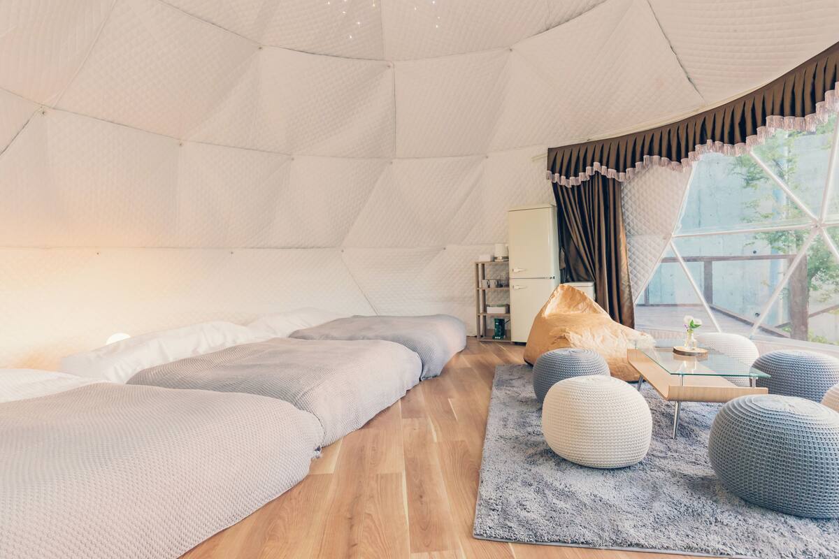 A modern, spacious room with a large bed, a glass coffee table, and a view through a large window.