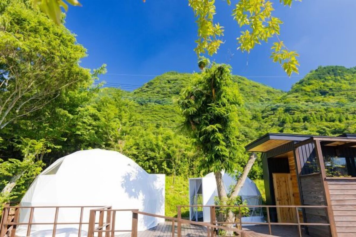 A white dome-shaped structure, possibly a yurt, surrounded by a wooden deck and a small building with a sloped roof.